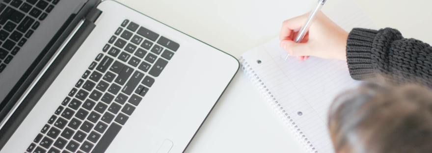 Person in with pen and paper in front of open laptop, ready to take notes.